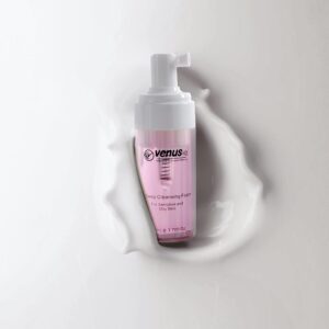 Pink foaming cleanser bottle with pump and liquid splash on white background.