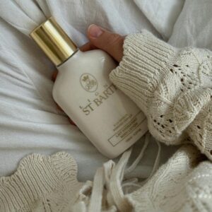 A hand in a sweater holds a luxury body lotion bottle on a white background.